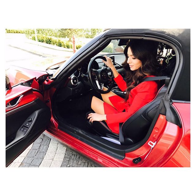 Melisa Aslı Pamuk in a red dress in her red car.